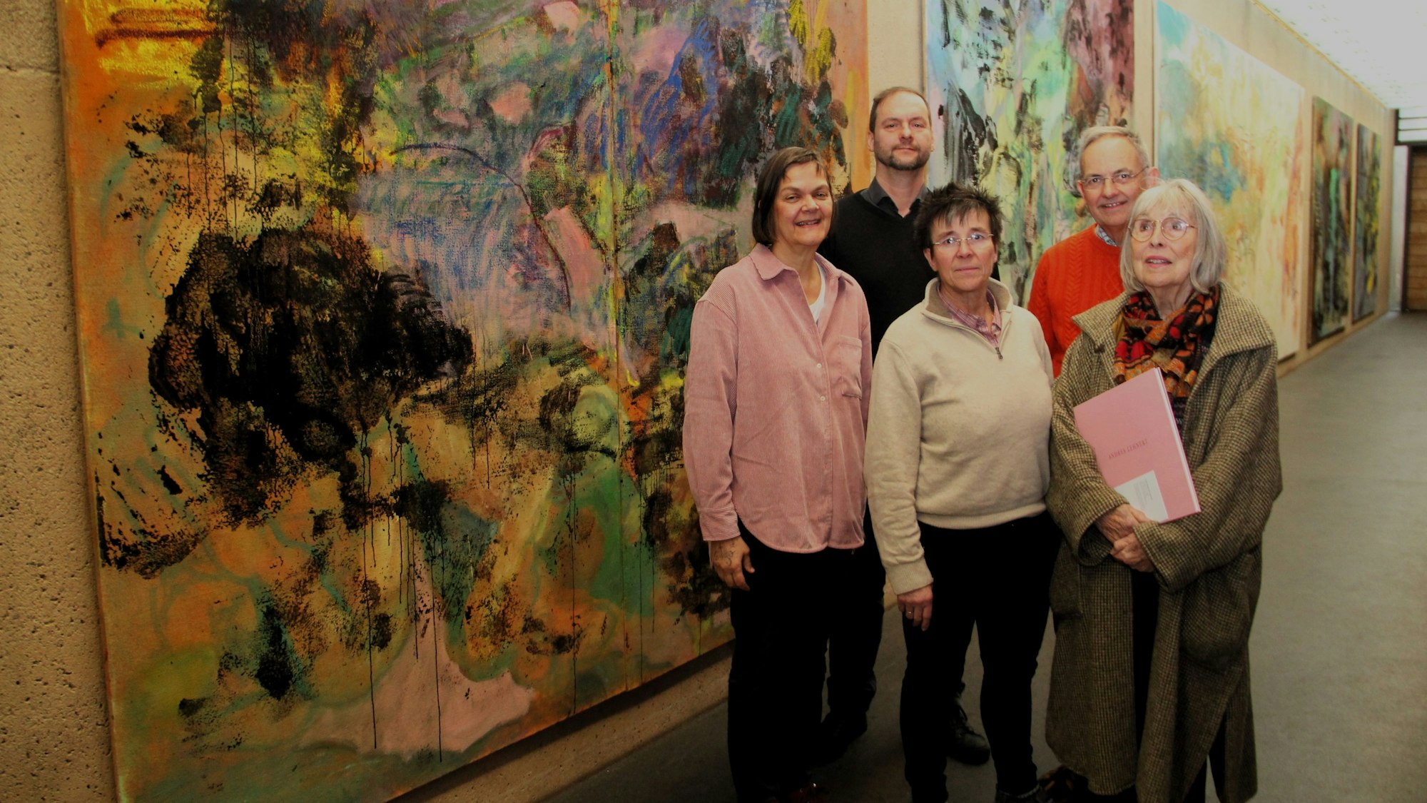 Fünf Personen stehen vor mehreren großen Gemälden.