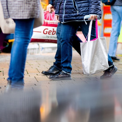 Menschen gehen mit Einkaufstaschen durch die Fußgängerzone einer Innenstadt.
