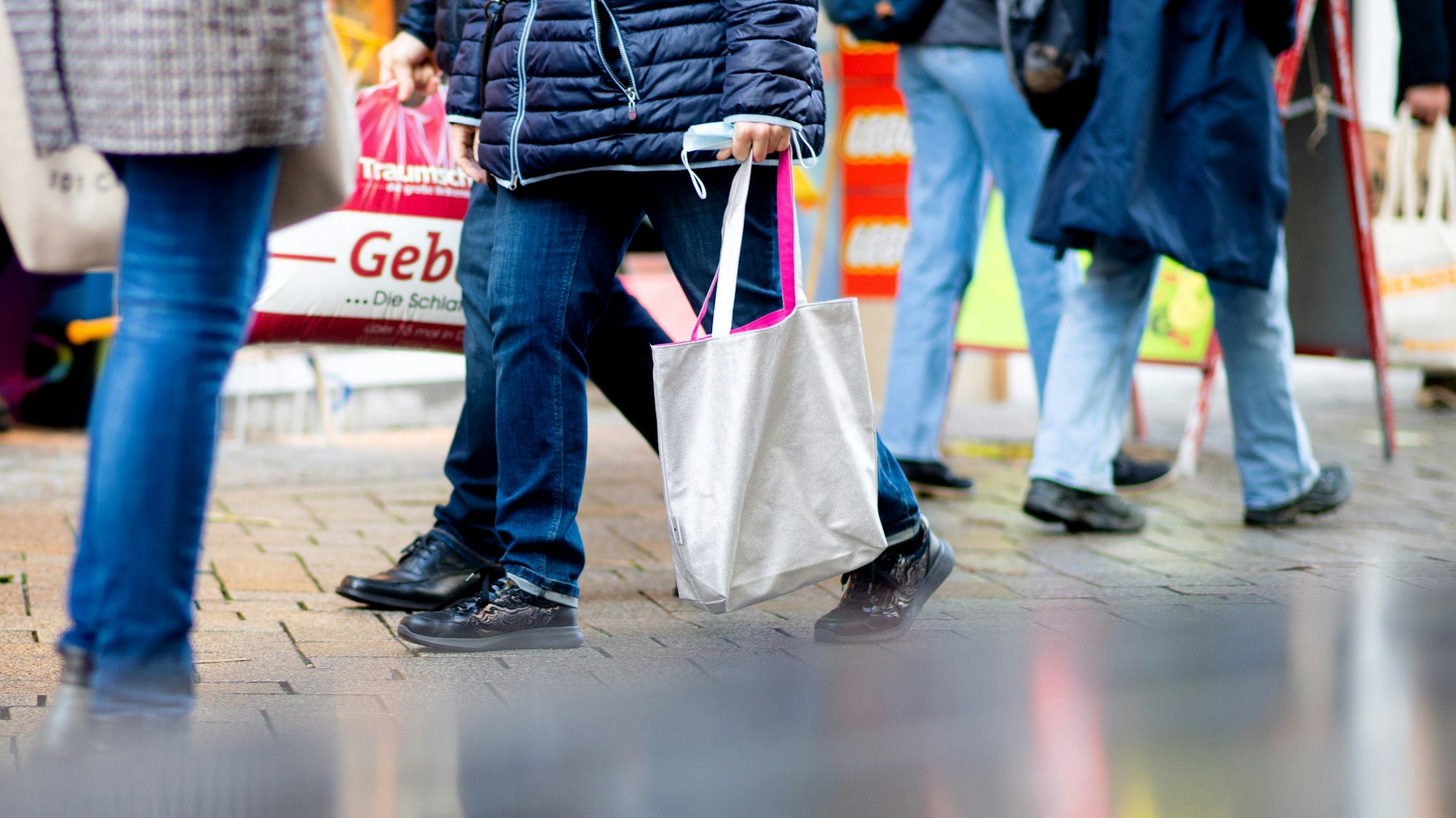 Menschen gehen mit Einkaufstaschen durch die Fußgängerzone einer Innenstadt.
