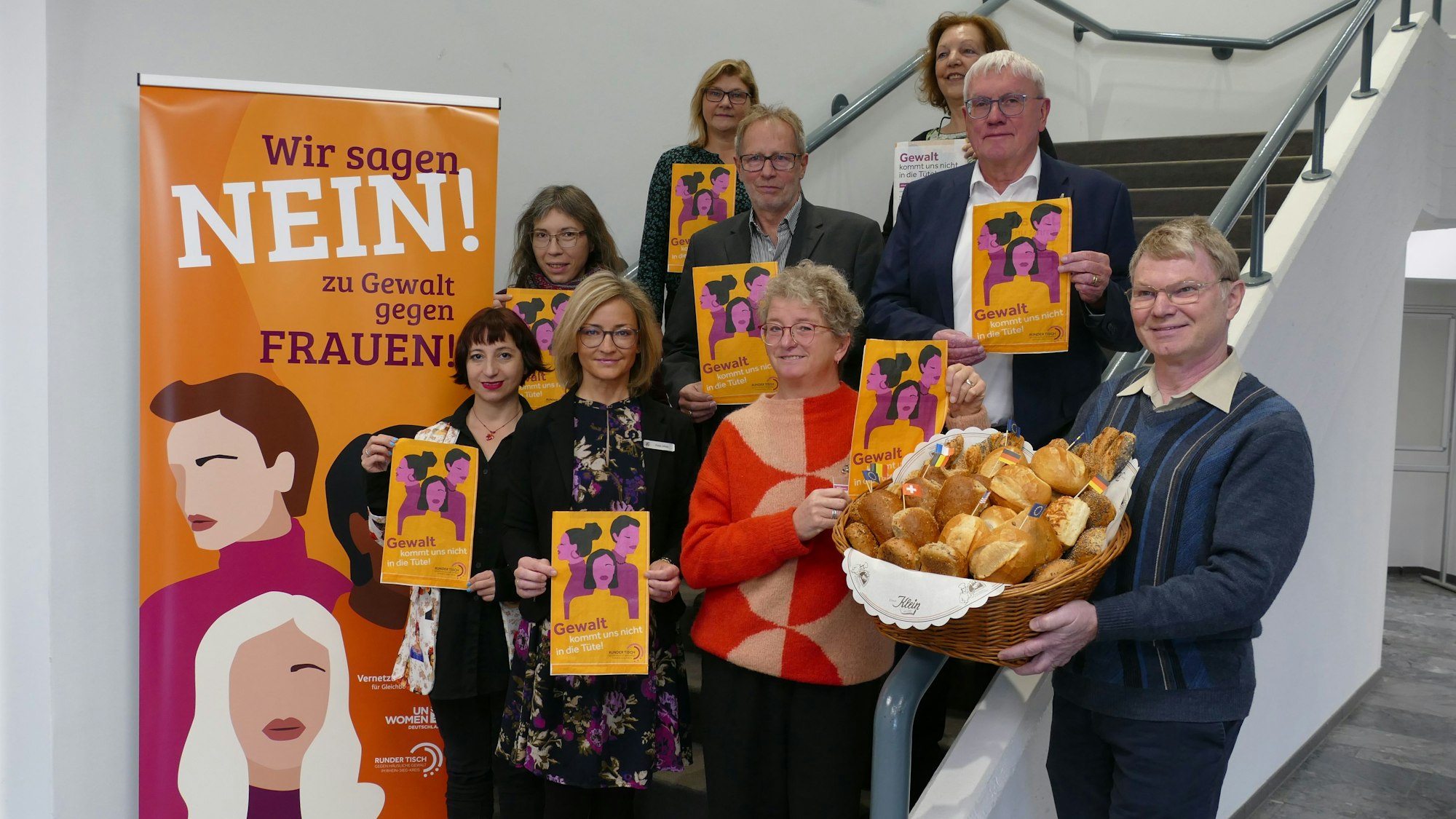 Mehrere Menschen stehen auf einer Treppe und halten Tüten sowie einen Brötchenkorb hoch.