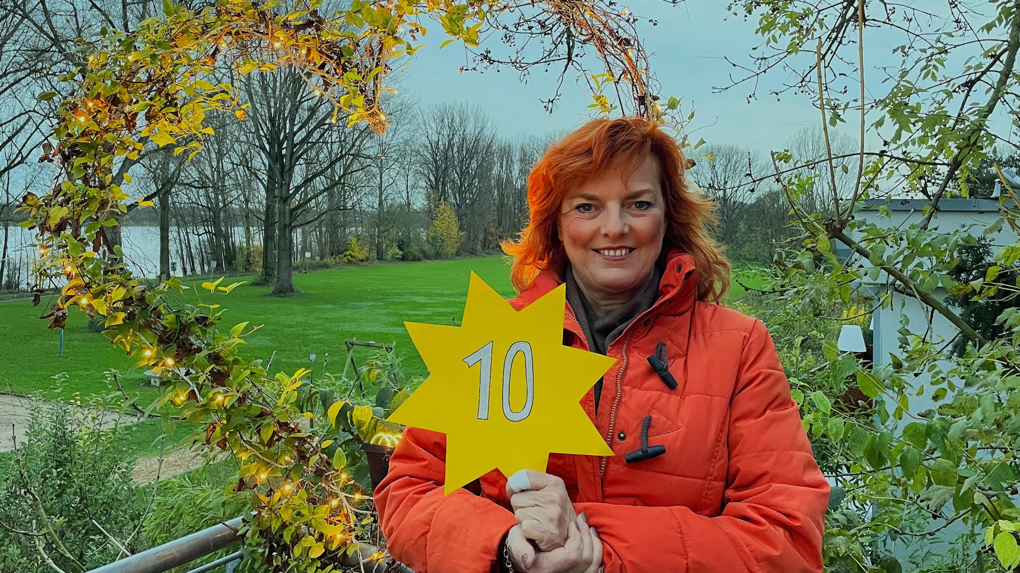 Eine Frau mit roten Haaren steht auf einem Balkon und hält einen Stern mit der Nr. 10 in der Hand.