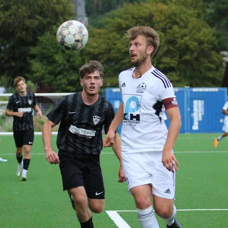 Zwei Fußballer fixieren mit den Augen den herannahenden Ball.
