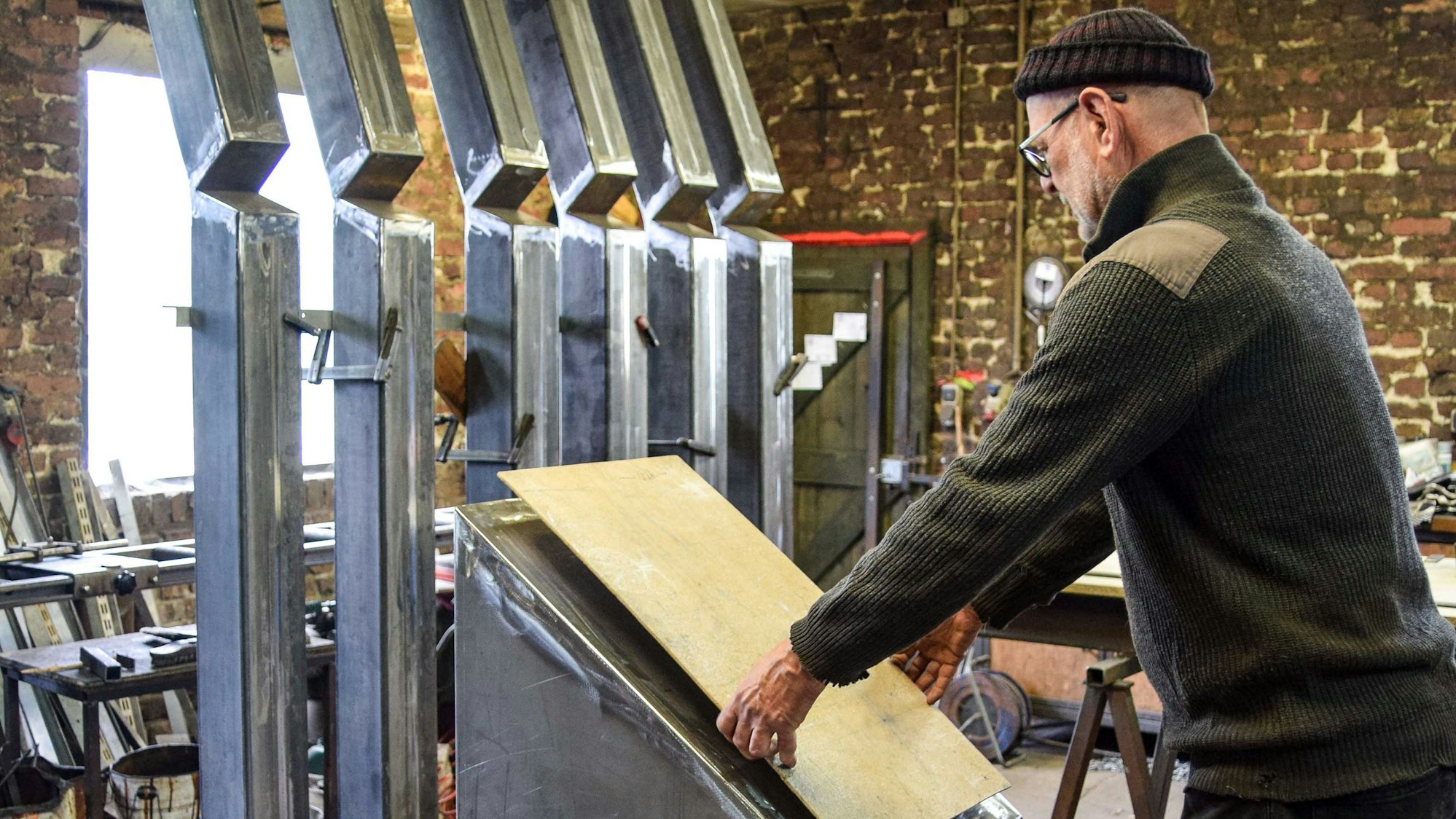 Ein Mann hält eine Holzplatte an die zentrale Stele, im Hintergrund sind die sechs Säulen zu sehen.