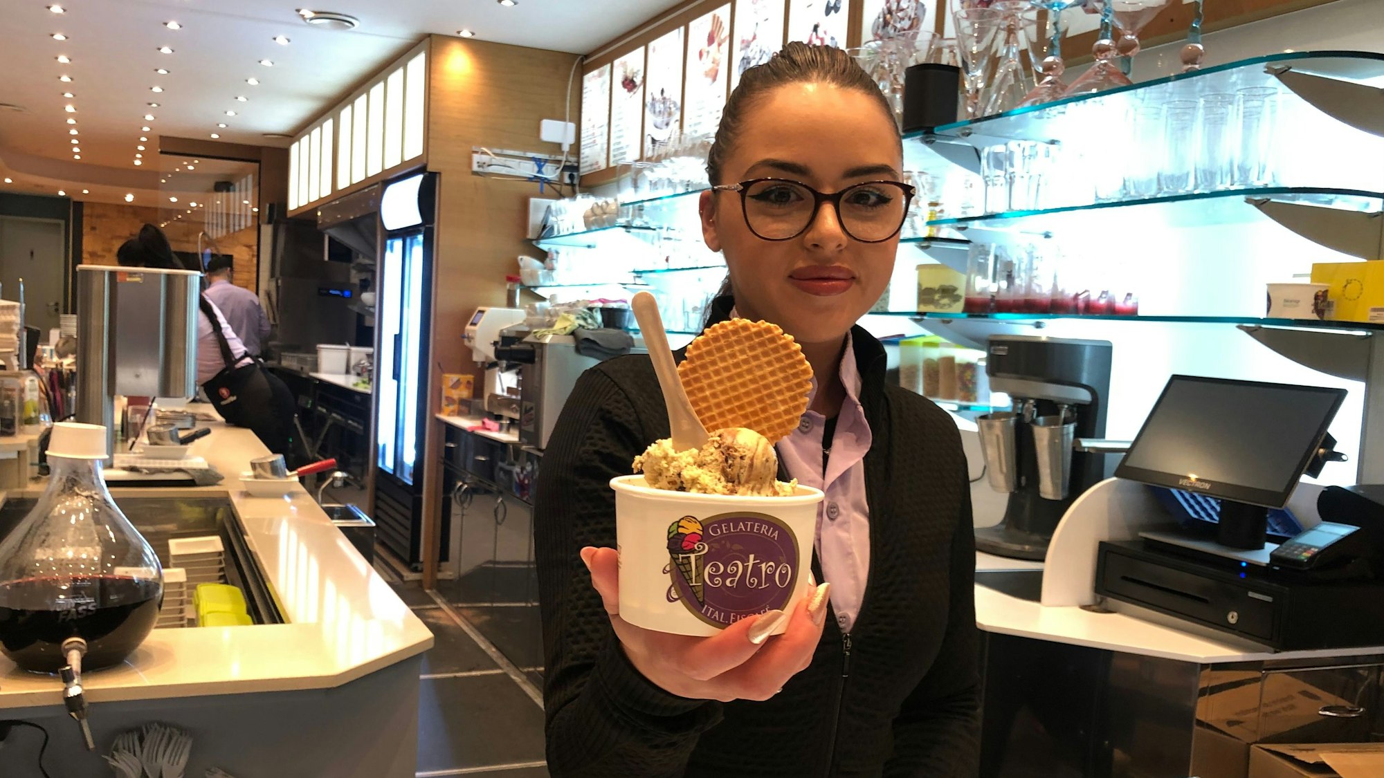 Eine junge Frau reicht einen Becher mit Eis über die Theke.