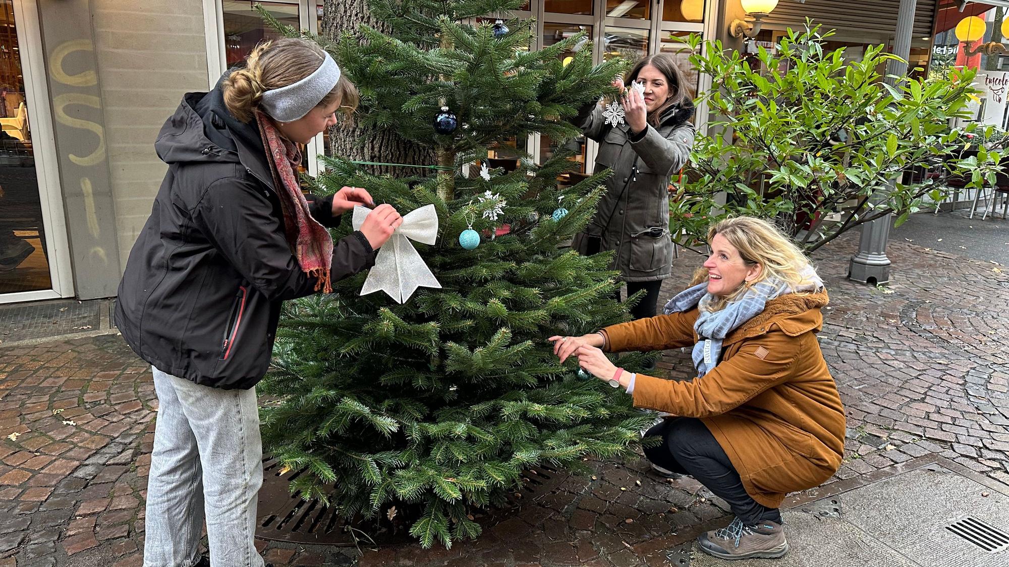 Die Holzgasse wird mit Weihnachtsbäumen verschönert. Von links: Pfadfinderin Emma Quadt vom Stamm Exodus, Heike Krudewig und Sabine Elfgen.