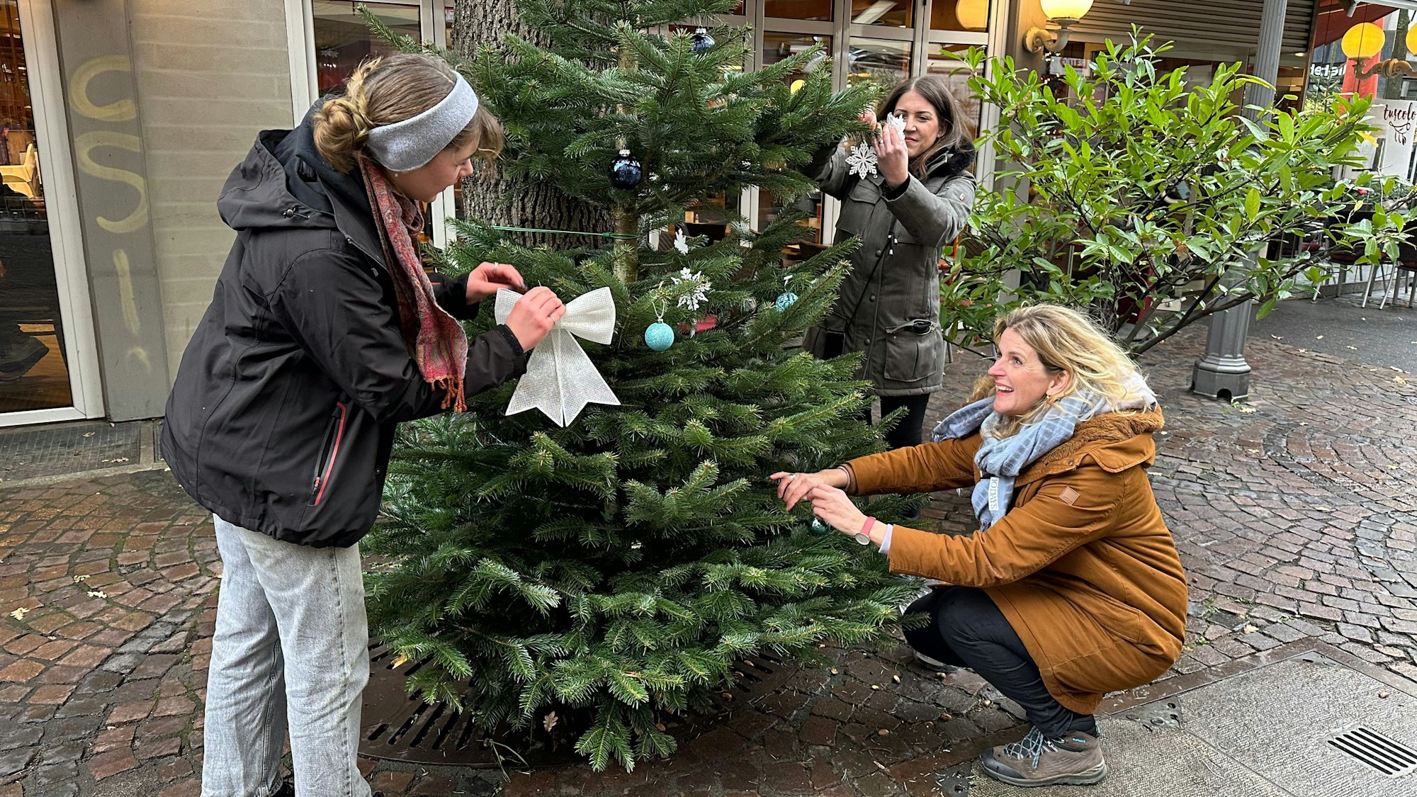 Die Holzgasse wird mit Weihnachtsbäumen verschönert. Von links: Pfadfinderin Emma Quadt vom Stamm Exodus, Heike Krudewig und Sabine Elfgen.