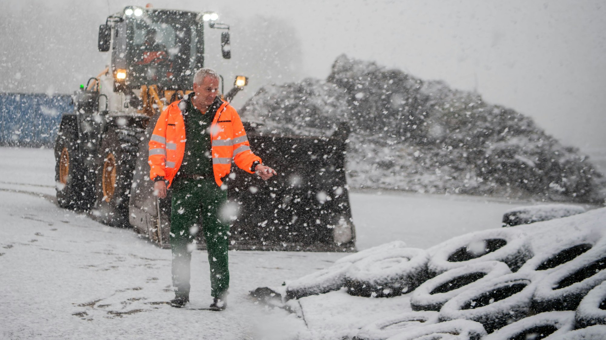 Ein Mann in Warnweste steht draußen neben Reifen, während es schneit.