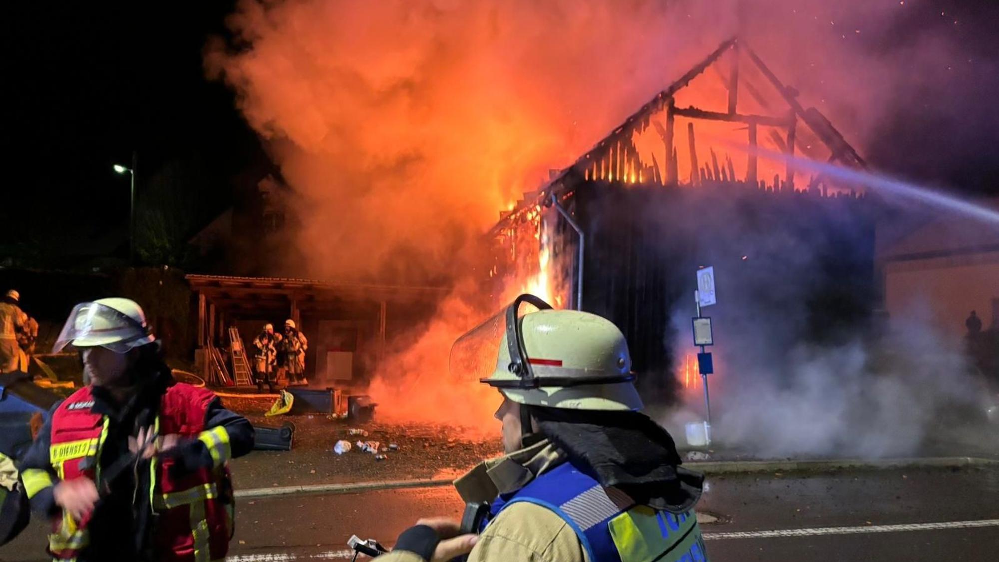 Eine brennende Scheune, im Vordergrund Feuerwehrleute.