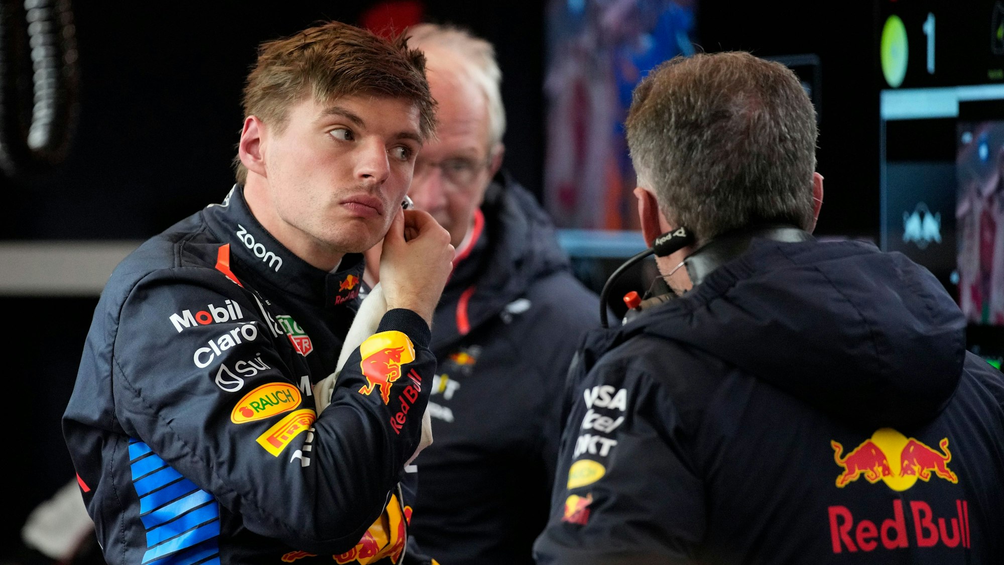 Max Verstappen trägt seinen Rennanzug und nimmt einen Kopfhörer aus seinem linken Ohr.
