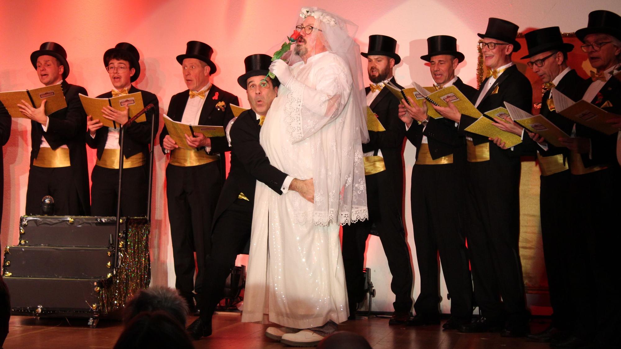 Auf dem Bild sind ein als Braut verkleideter Mann und viele Chorsänger im Frack zu sehen.