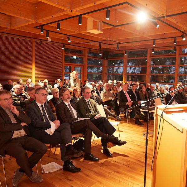 Der Vorsitzende der Jury steht am Rednerpult, vor ihm sitzen die Gäste.