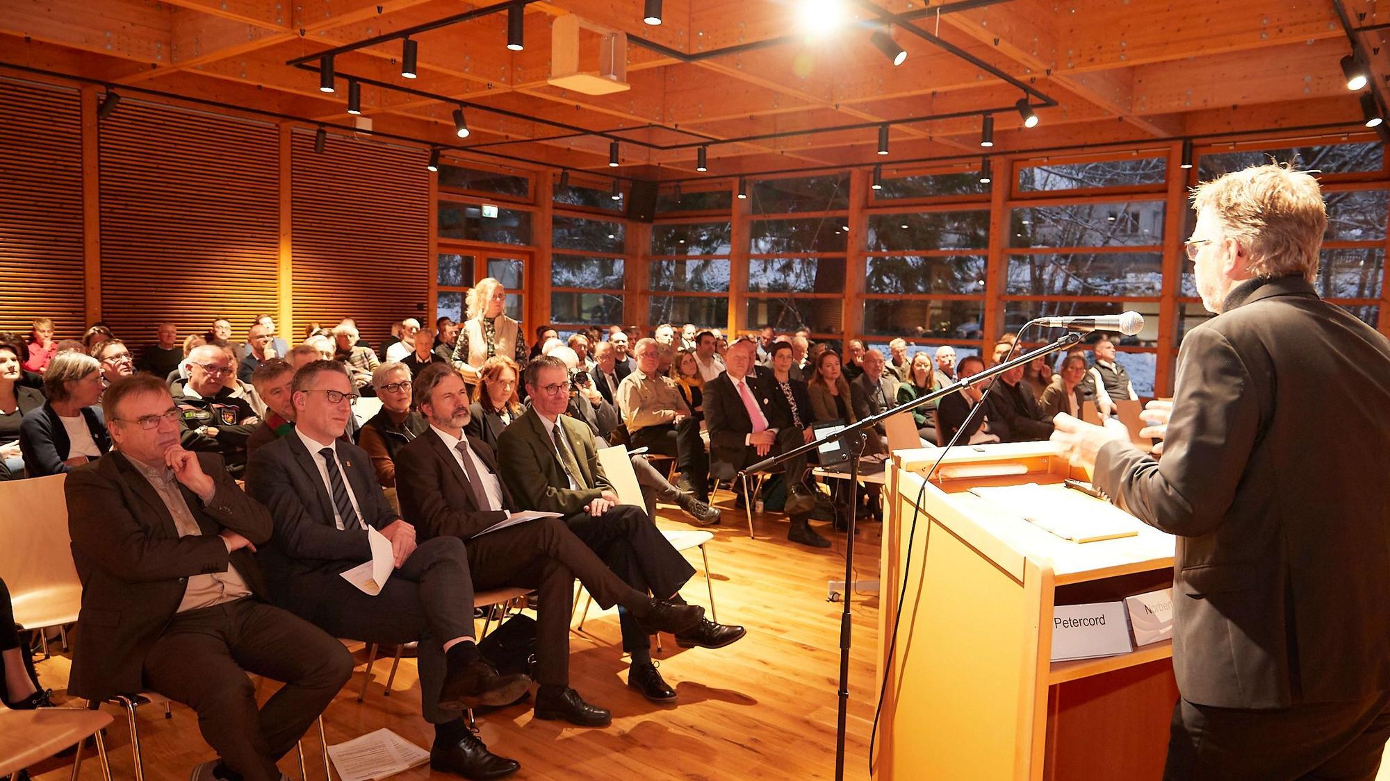 Der Vorsitzende der Jury steht am Rednerpult, vor ihm sitzen die Gäste.