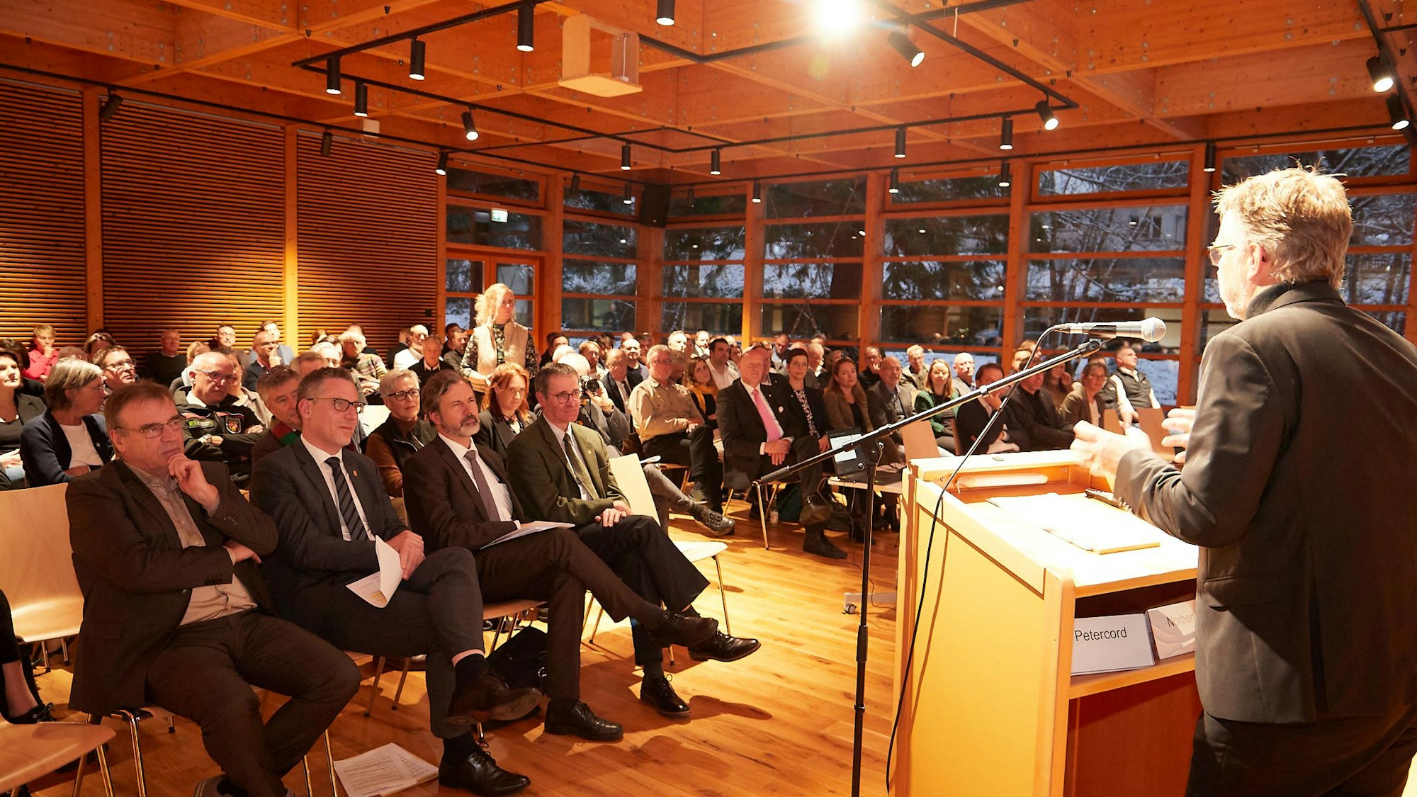 Der Vorsitzende der Jury steht am Rednerpult, vor ihm sitzen die Gäste.