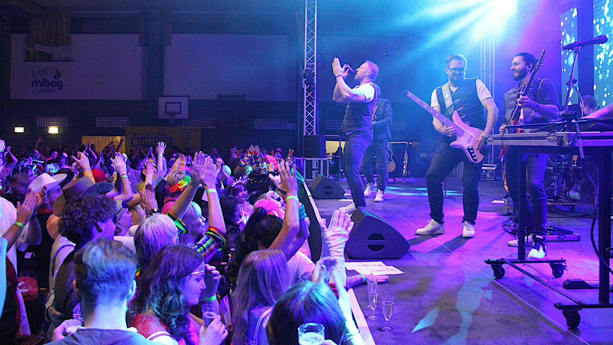 Auf einer blau ausgeleuchteten Bühne spielt die Band, vor der Bühne klatscht und singt das zum Teil kostümierte Publikum.