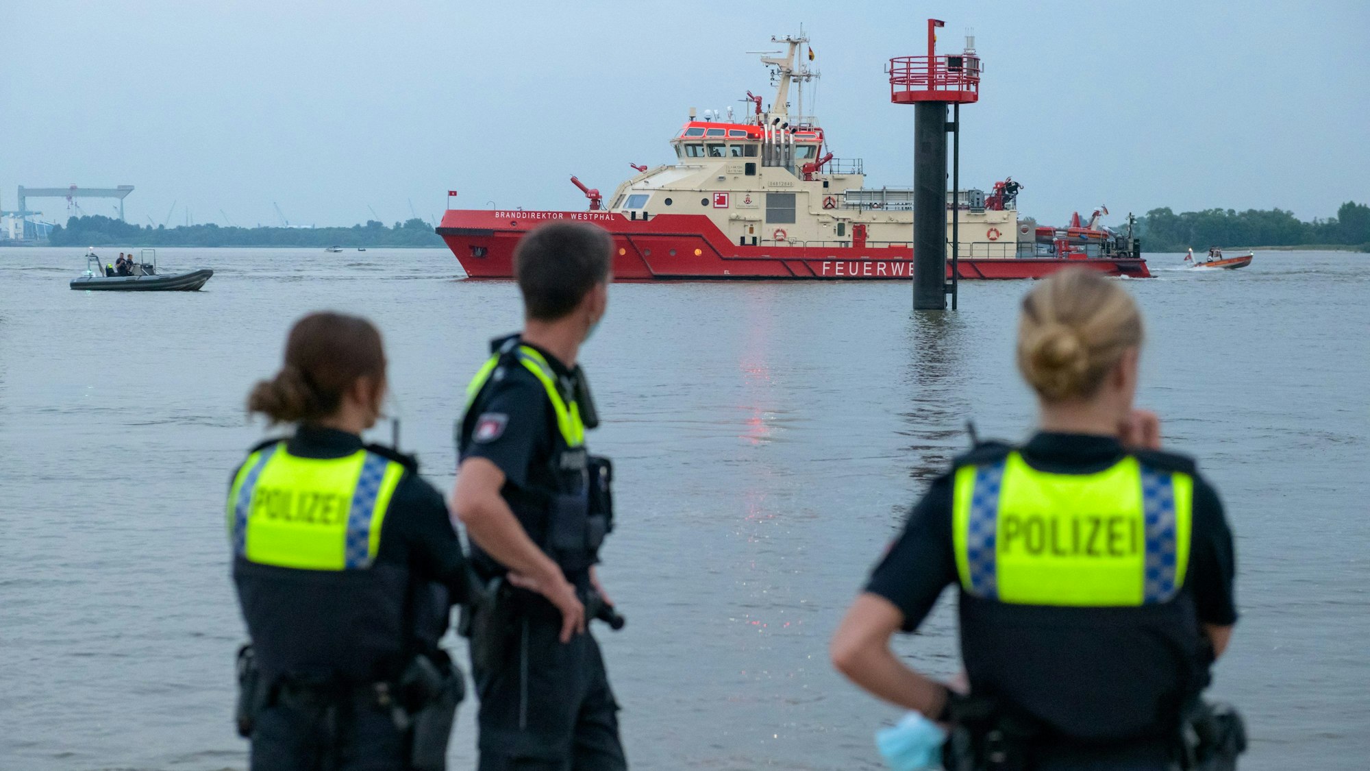 Polizisten beobachten vom Strand aus die Suche auf dem Wasser an der neben Kleinbooten auch das Löschboot «Branddirektor Westphal» beteiligt ist. (Archivbild)