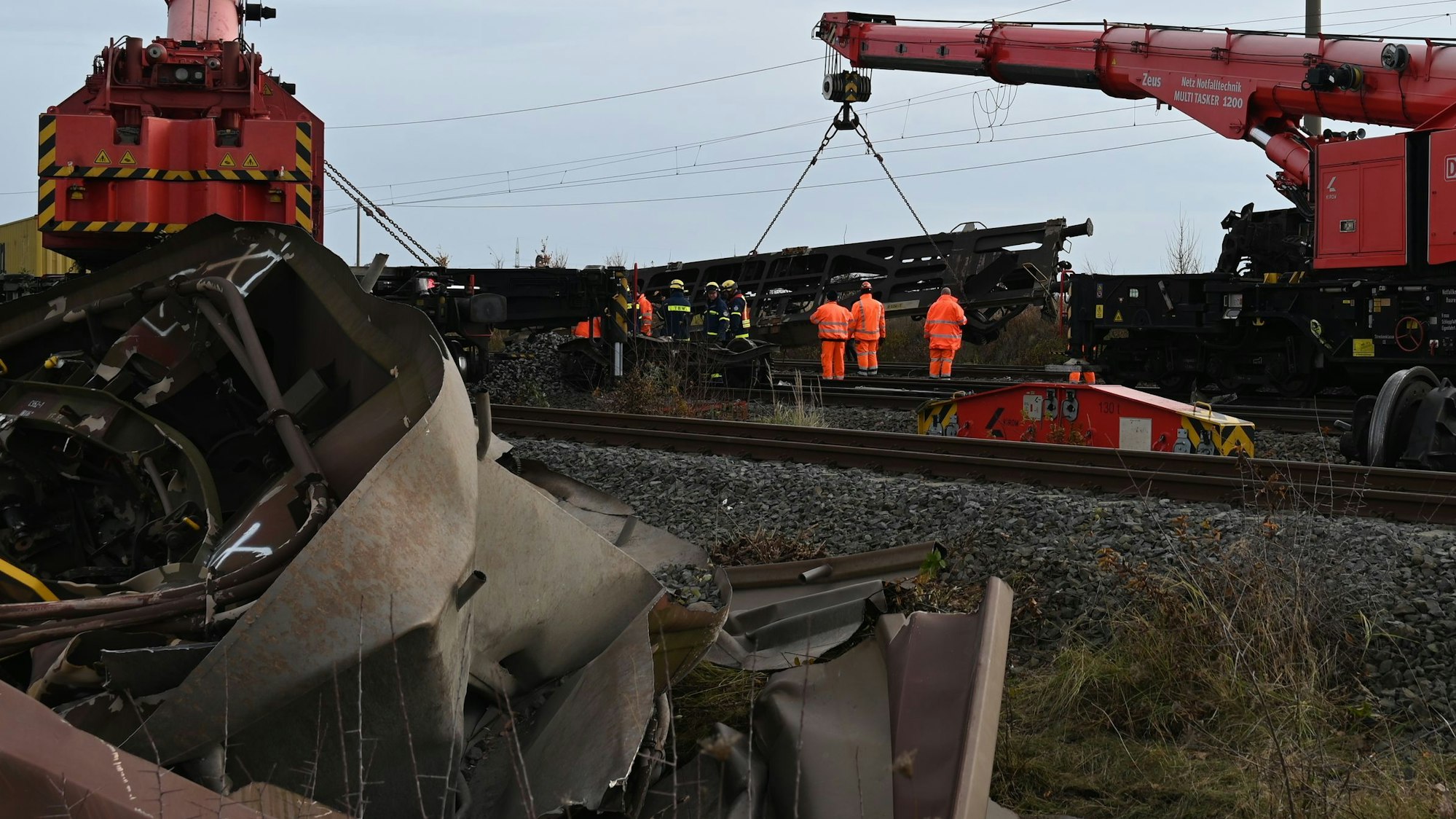 Das Bild zeigt mehrere Arbeiter auf den Gleisen und ein Kran, an dem ein Waggon hängt.