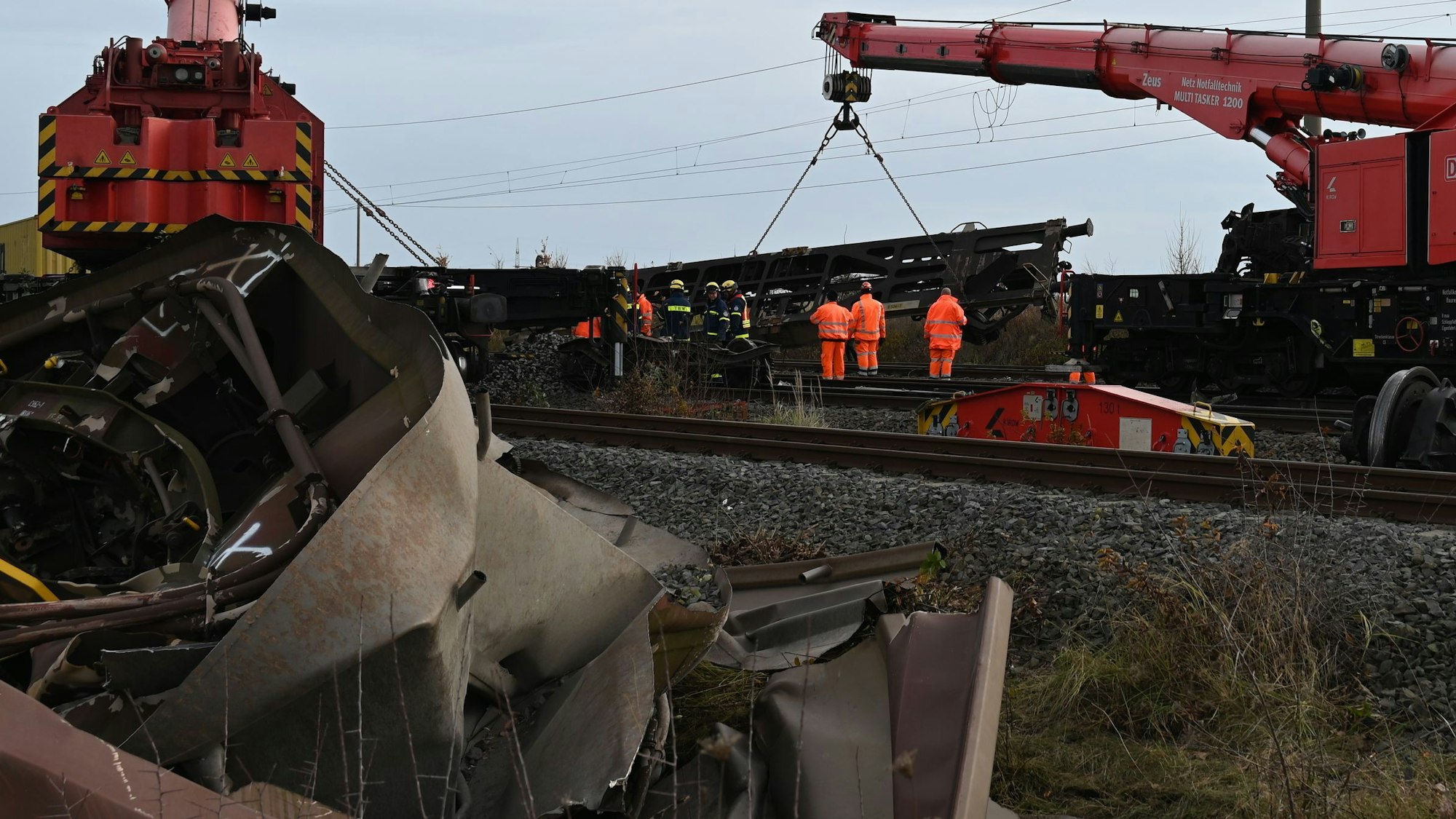 Das Bild zeigt mehrere Arbeiter auf den Gleisen und ein Kran, an dem ein Waggon hängt.