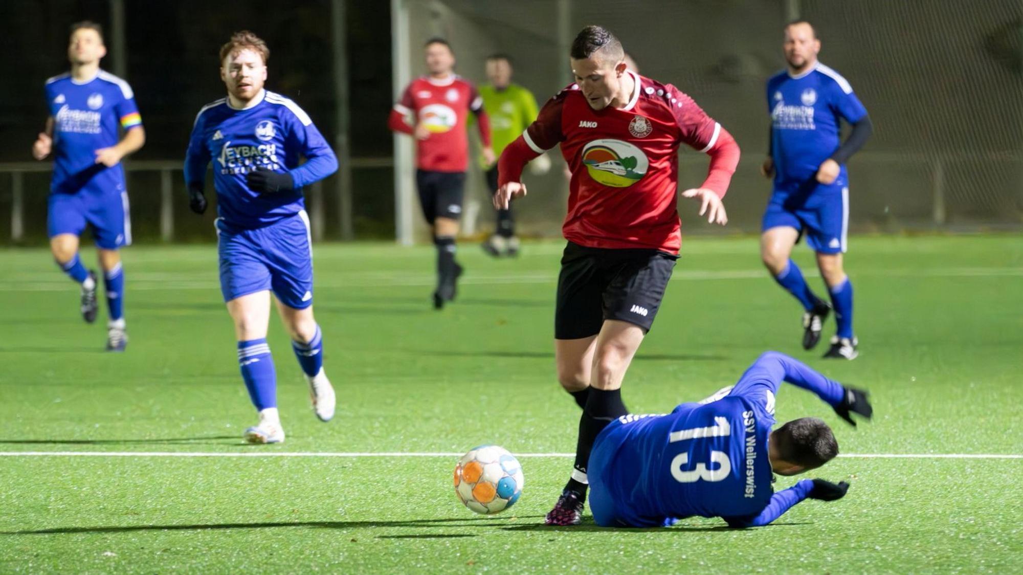 Ein Fußballer legt den Ball an einem auf dem Boden liegenden Gegner vorbei.