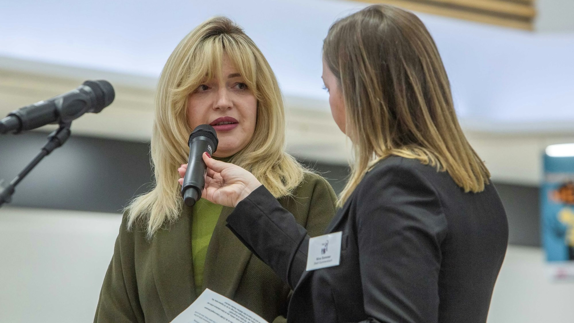 Katharina Falkenberg spricht auf einer Bühne in ein Mikrofon, das ihr eine andere Frau hinhält.