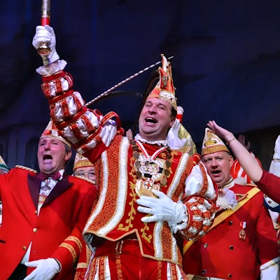 Mit weiteren Karnevalisten steht der Zülpicher Karnevalsprinz in seinem rot-weißen Prinzenkostüm auf der Bühne und grüßt ins Publikum.