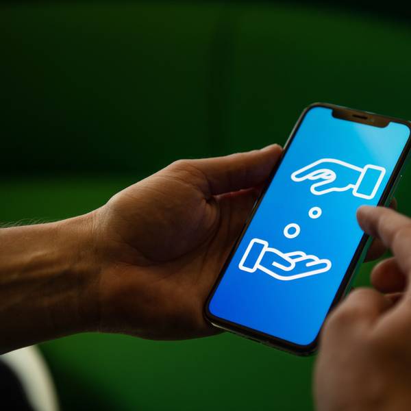 Ein Mann hält ein Handy in den Händen. Auf dem Display sind zwei Hände zu sehen, die sich Geld geben.