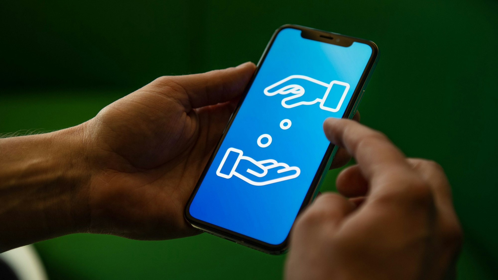 Ein Mann hält ein Handy in den Händen. Auf dem Display sind zwei Hände zu sehen, die sich Geld geben.