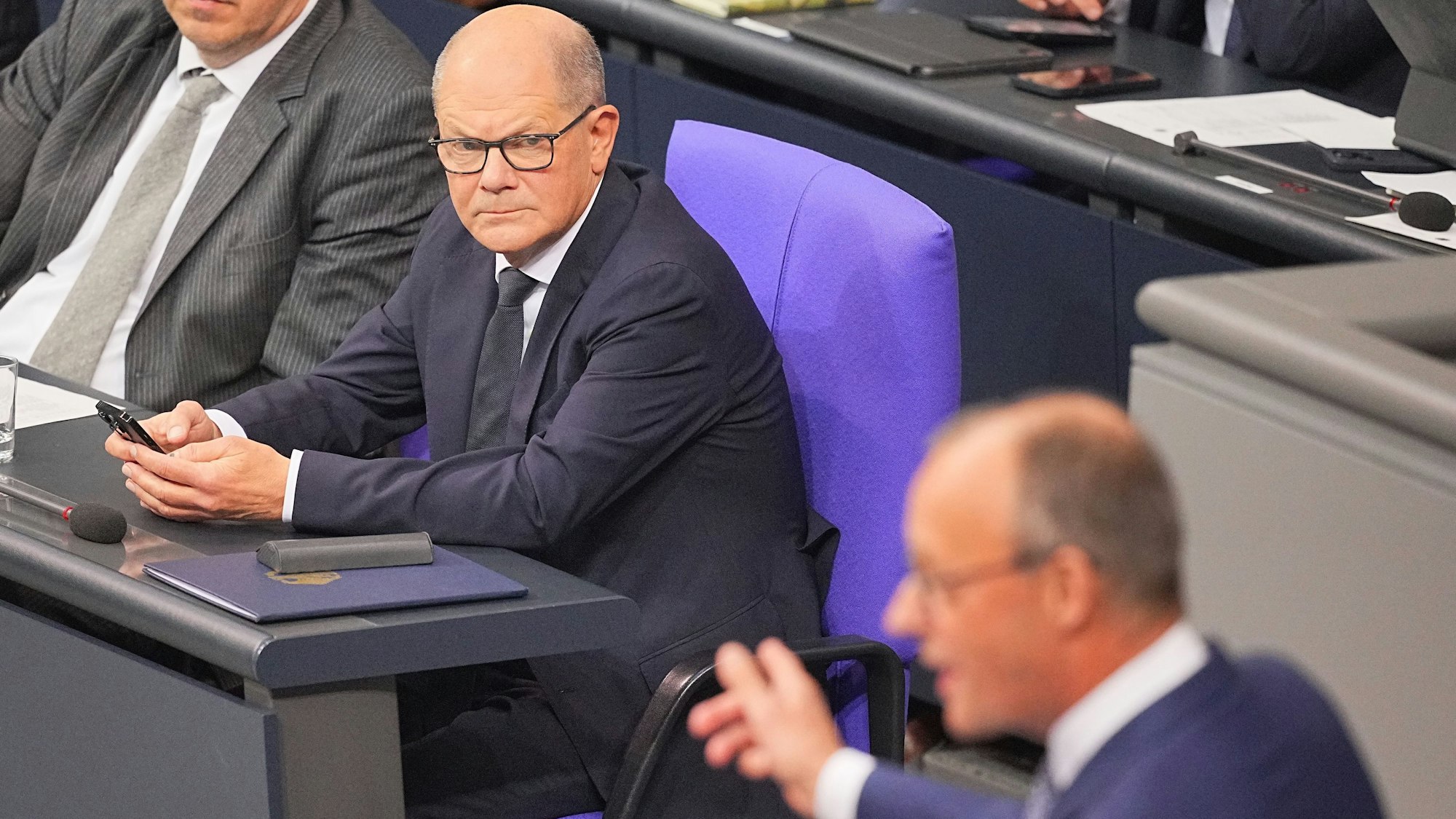 Olaf Scholz beobachtet eine Rede von Friedrich Merz im Bundestag.