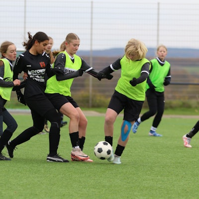 Fußballerinnen im Zweikampf. Da beide Mannschaften schwarze Trikots und Hosen trugen, mussten die Gastgeberinnen grellgrüne Leibchen überziehen.