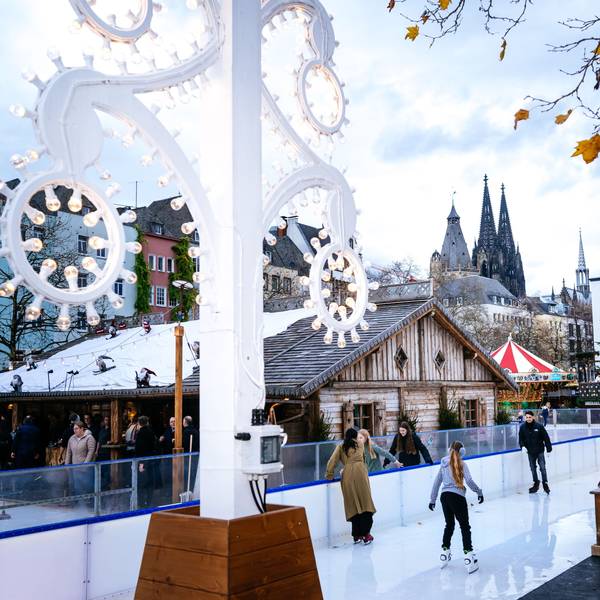 Leute fahren auf einer Eisbahn Schlittschuh. Im Hintergrund ist der Kölner Dom zu sehen.