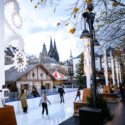 Leute fahren auf einer Eisbahn Schlittschuh. Im Hintergrund ist der Kölner Dom zu sehen.