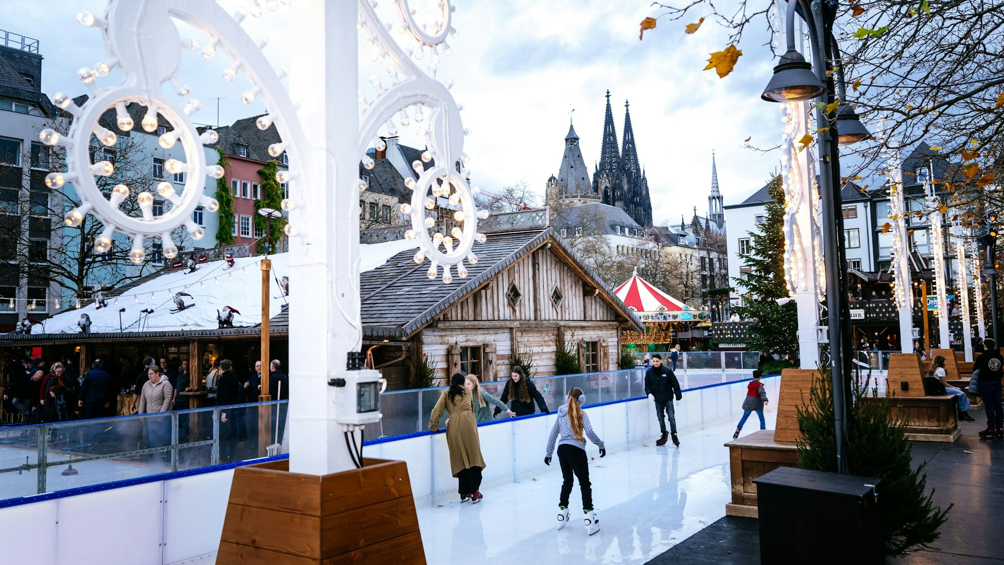 Leute fahren auf einer Eisbahn Schlittschuh. Im Hintergrund ist der Kölner Dom zu sehen.