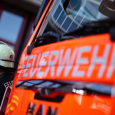 Das Foto zeigt einen Feuerwehrmann vor einem Einsatzfahrzeug mit dem Schriftzug „Feuerwehr“.
