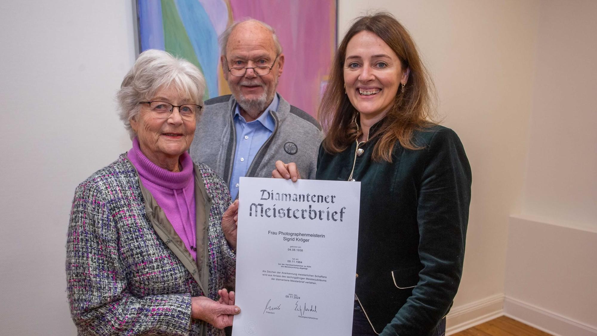 Von Waldbröls Bürgermeisterin Larissa Weber (rechts) hat Sigrid Kröger den diamantenen Meisterbrief der Handwerkskammer zu Köln erhalten, auch Ehemann Klaus freut sich darüber.