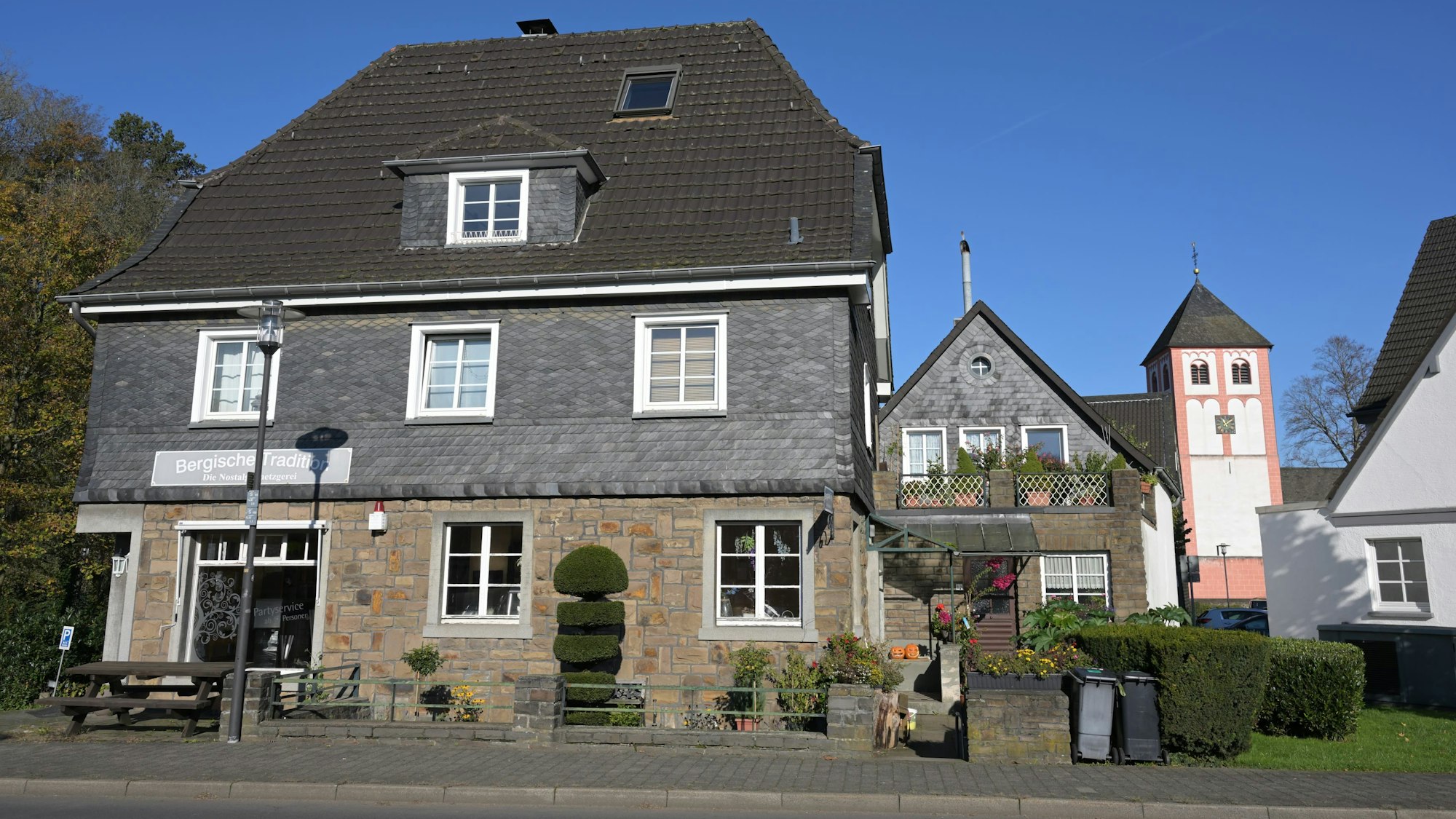 Ein bergisches Fachwerkhaus mit Ladenlokal, dahinter ein Kirchturm.