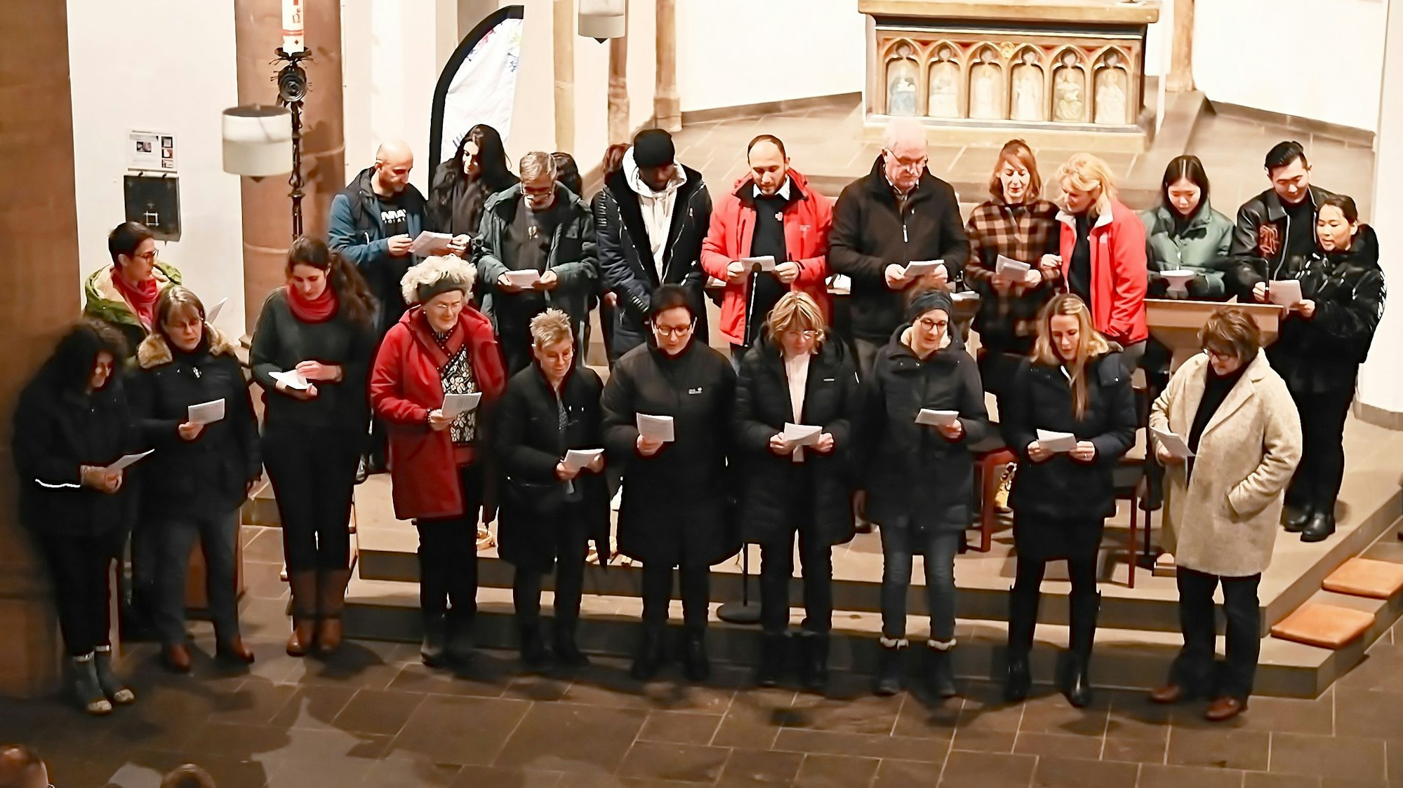 Sängerinnen und Sänger stehen gemeinsam im Altarraum der Kirche Marmagen und schauen auf Texthefte, die sie in den Händen halten.