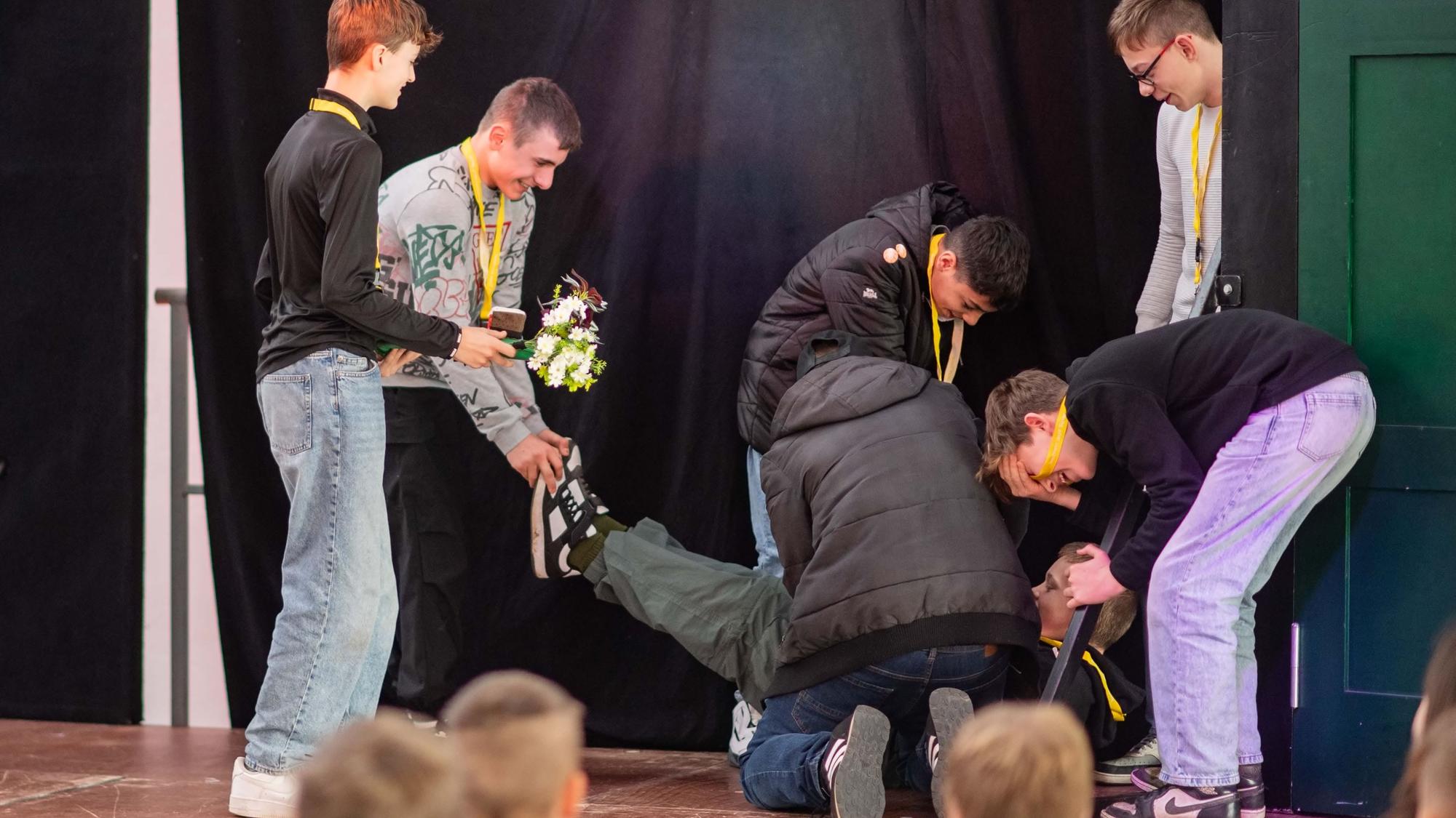 Das Bild zeigt sieben Schüler, die auf der Bühne ein Stück vorführen. Dabei lachen sie.