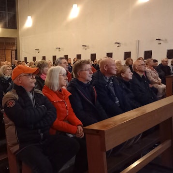 Ein Blick ins Pfarrzentrum, wo viele Menschen dicht gedrängt auf Bänken sitzen.