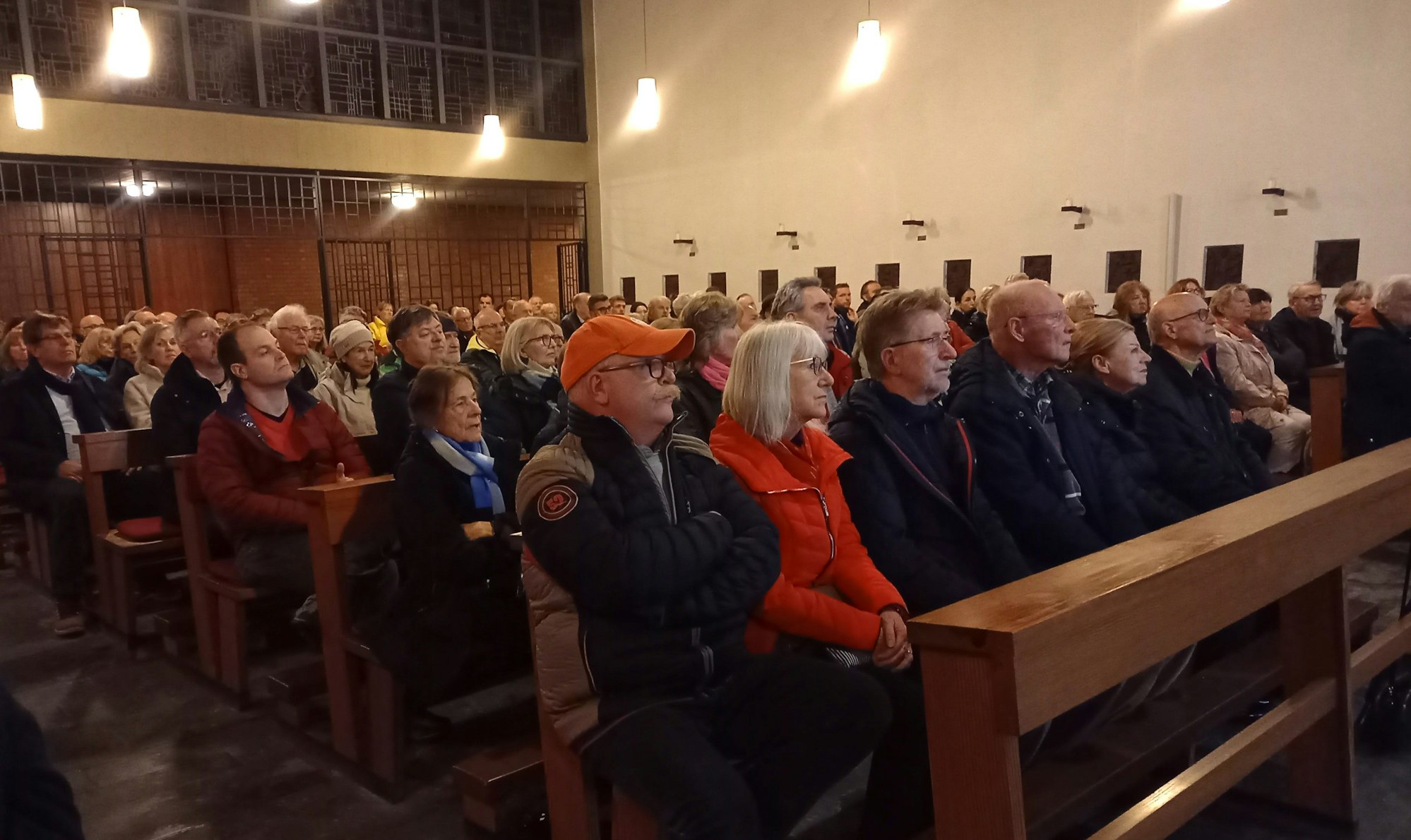 Ein Blick ins Pfarrzentrum, wo viele Menschen dicht gedrängt auf Bänken sitzen.