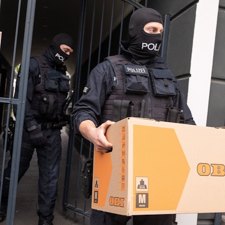 Ein Polizist trägt einen Karton aus einem Gebäude.