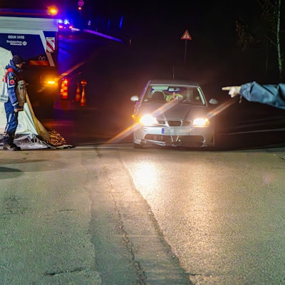 In der Dunkelheit rollt ein Auto auf einen Polizisten zu, der dem Fahrer mit energischem Handzeichen den Weg zur Kontrollstelle weist.