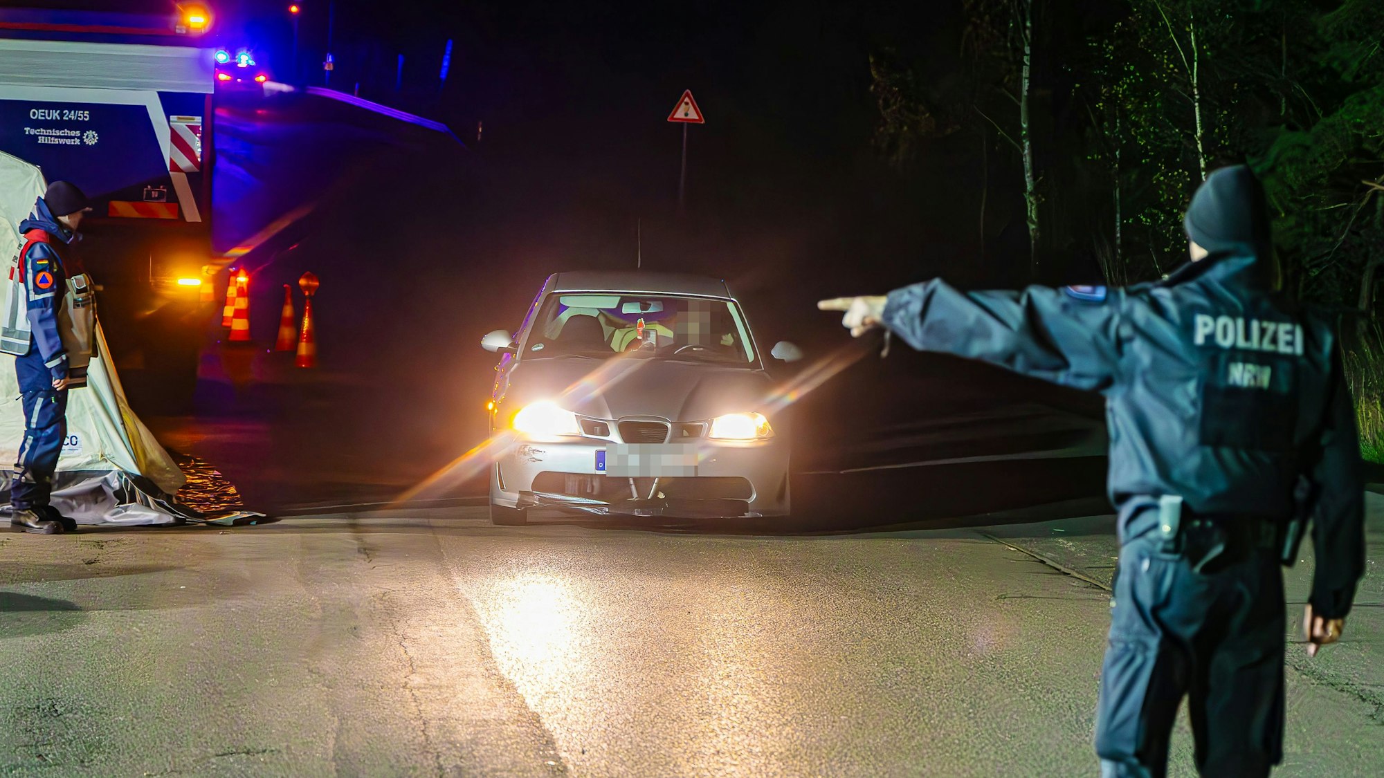 In der Dunkelheit rollt ein Auto auf einen Polizisten zu, der dem Fahrer mit energischem Handzeichen den Weg zur Kontrollstelle weist.