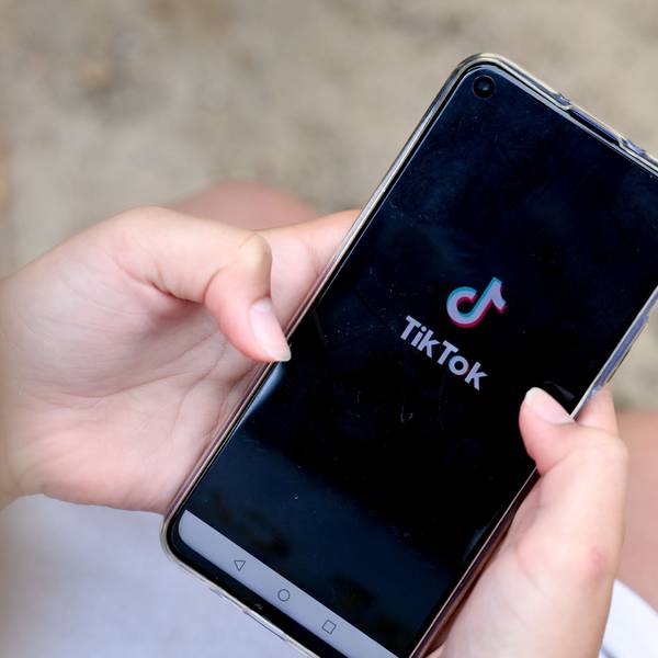 Ein Mädchen hält ein Smartphone in den Händen, auf dem das Logo von TikTok zu sehen ist.