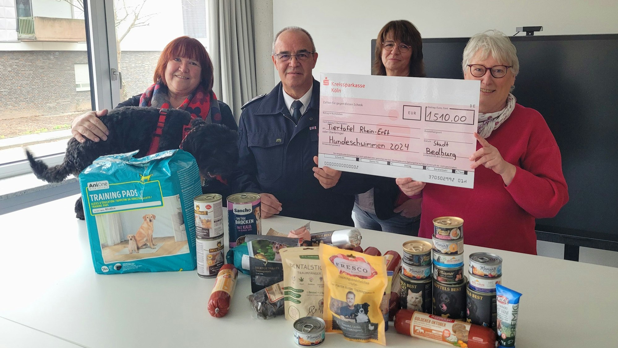 Vor den genannten Personen liegen Dosen, Tüten und Säcke mit Tierfutter auf einem Tisch.