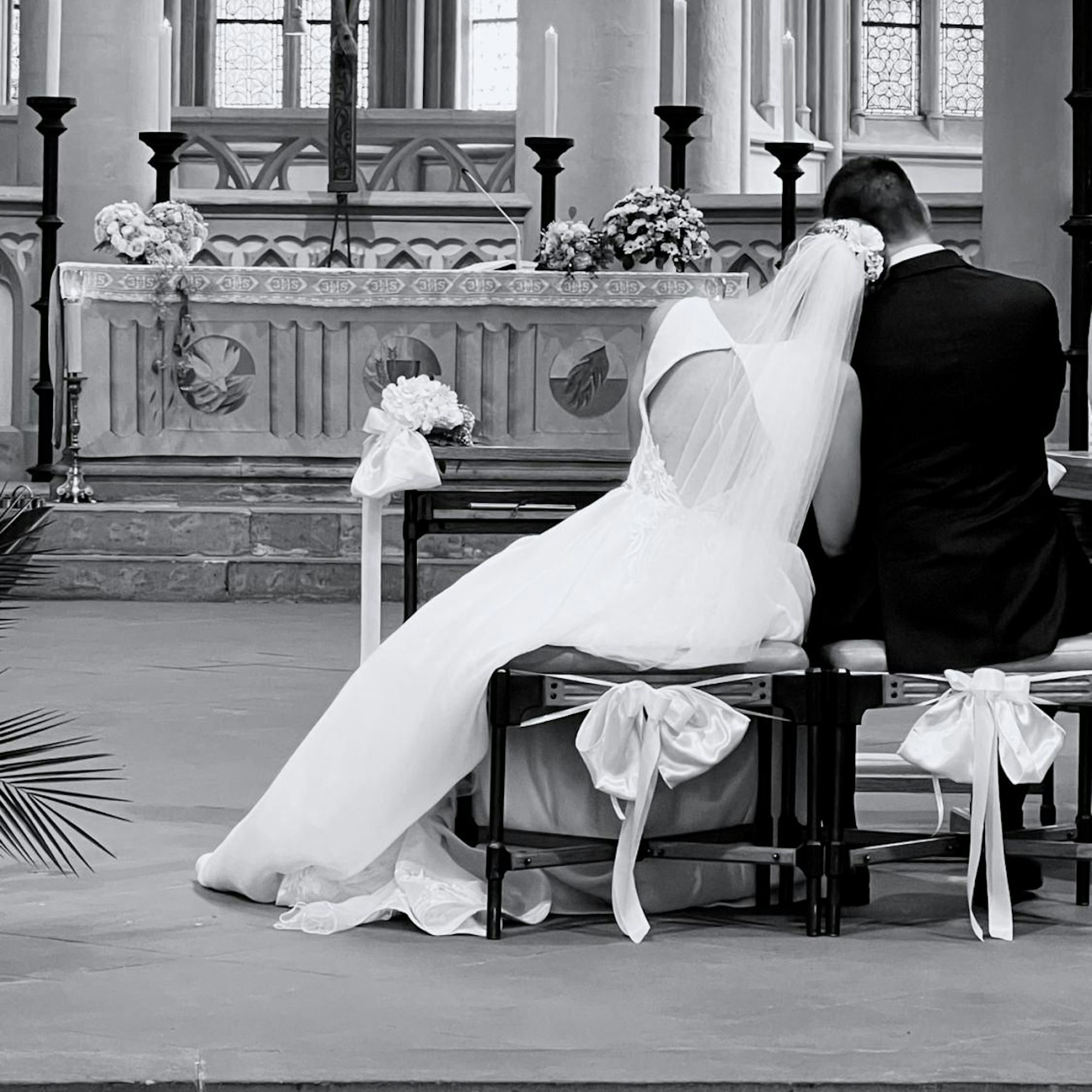 Eine Braut und ein Bräutigam sitzen aneinander gelehnt vor dem Altar.