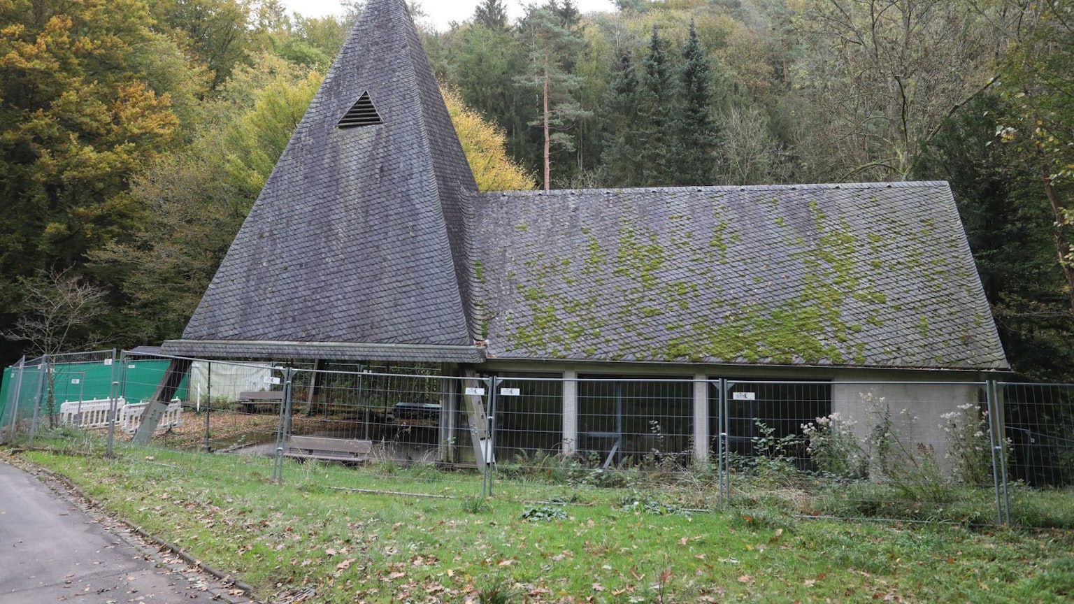 Eine Kapelle mit Turm und Trauerhalle, auf das Schieferdach wächst zum Teil Moos.