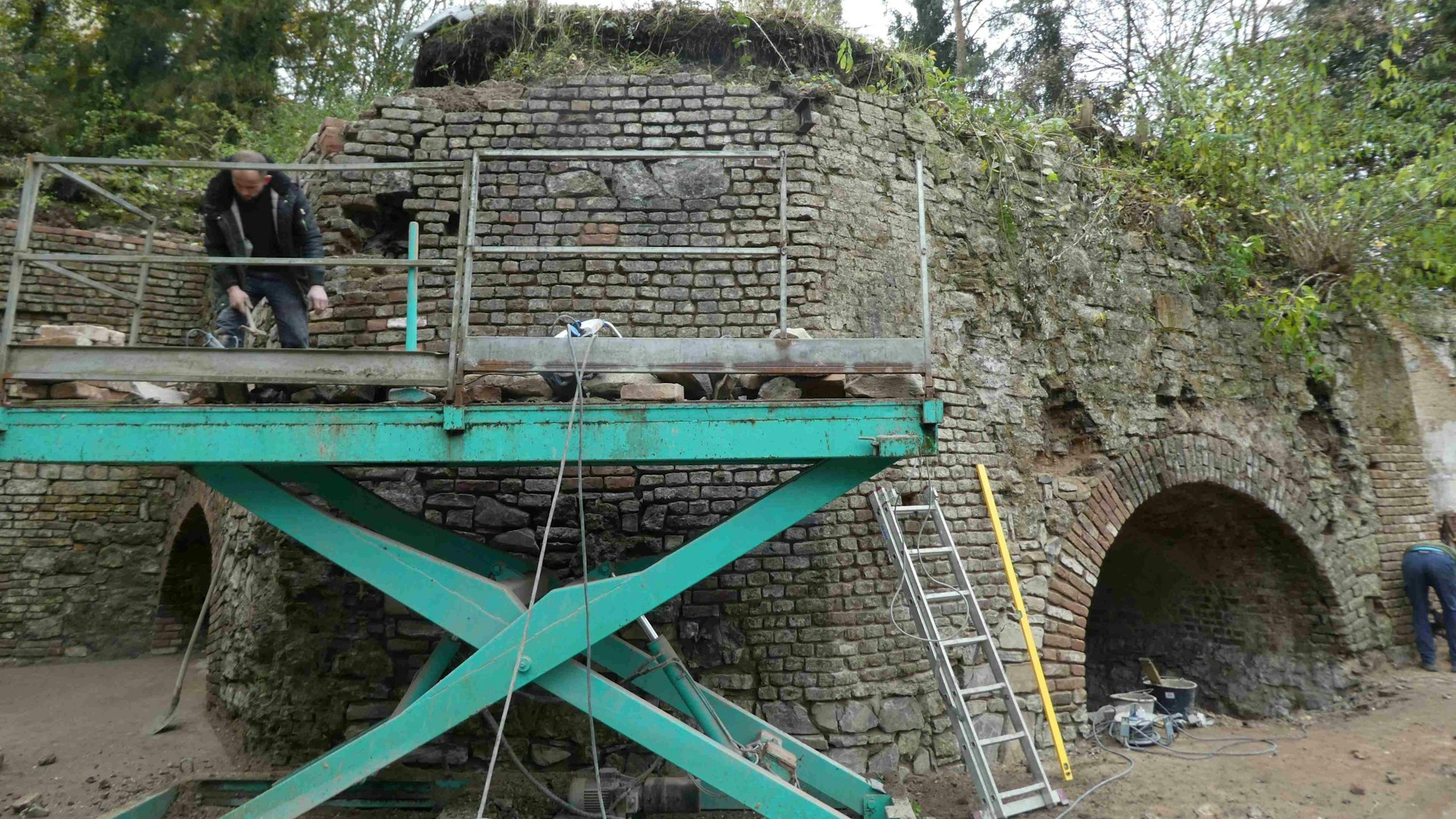 Ein Gerüst steht an einer Ziegelmauer. Darauf ein Handwerker.