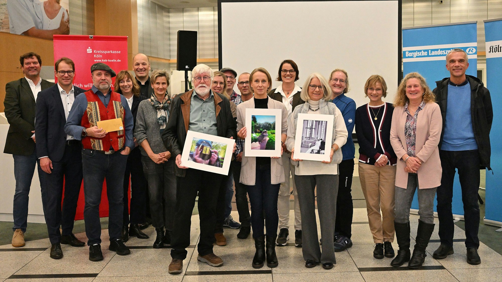 Preisträger des Fotowettbewerbs „Foto des Jahres 2024“ stehen mit Vertretern von Bergischer Landeszeitung, Kölner Stadt-Anzeiger und Wettbewerbspartner Kreissparkasse Köln am Mittwochabend (27.11.) bei der Preisverleihung in der Kassenhalle der Regionalfiliale der Kreissparkasse Köln Bergisch Gladbach.