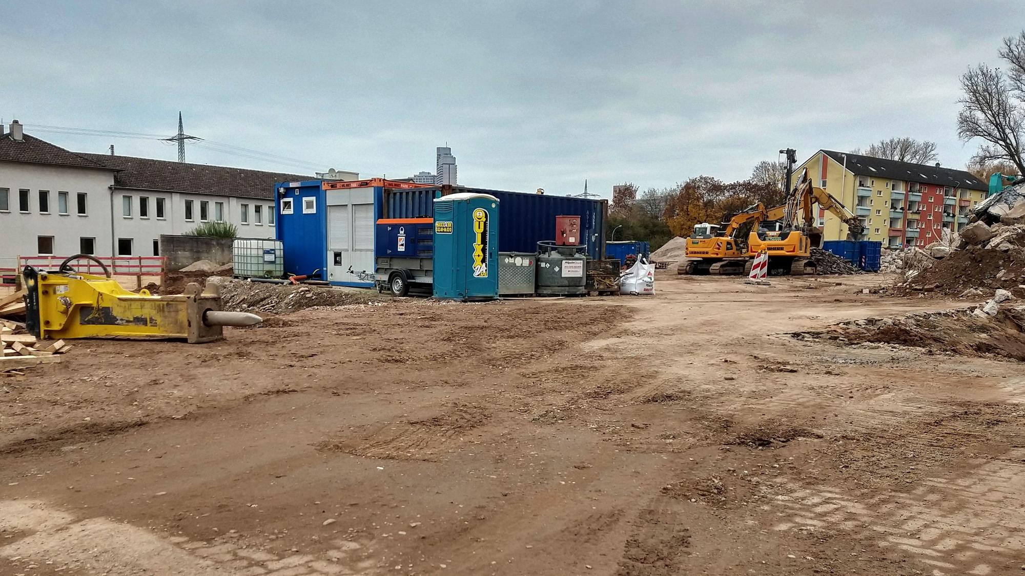Blick auf ein freies Baugrundstück mit Dixi-Klo und einem Bagger