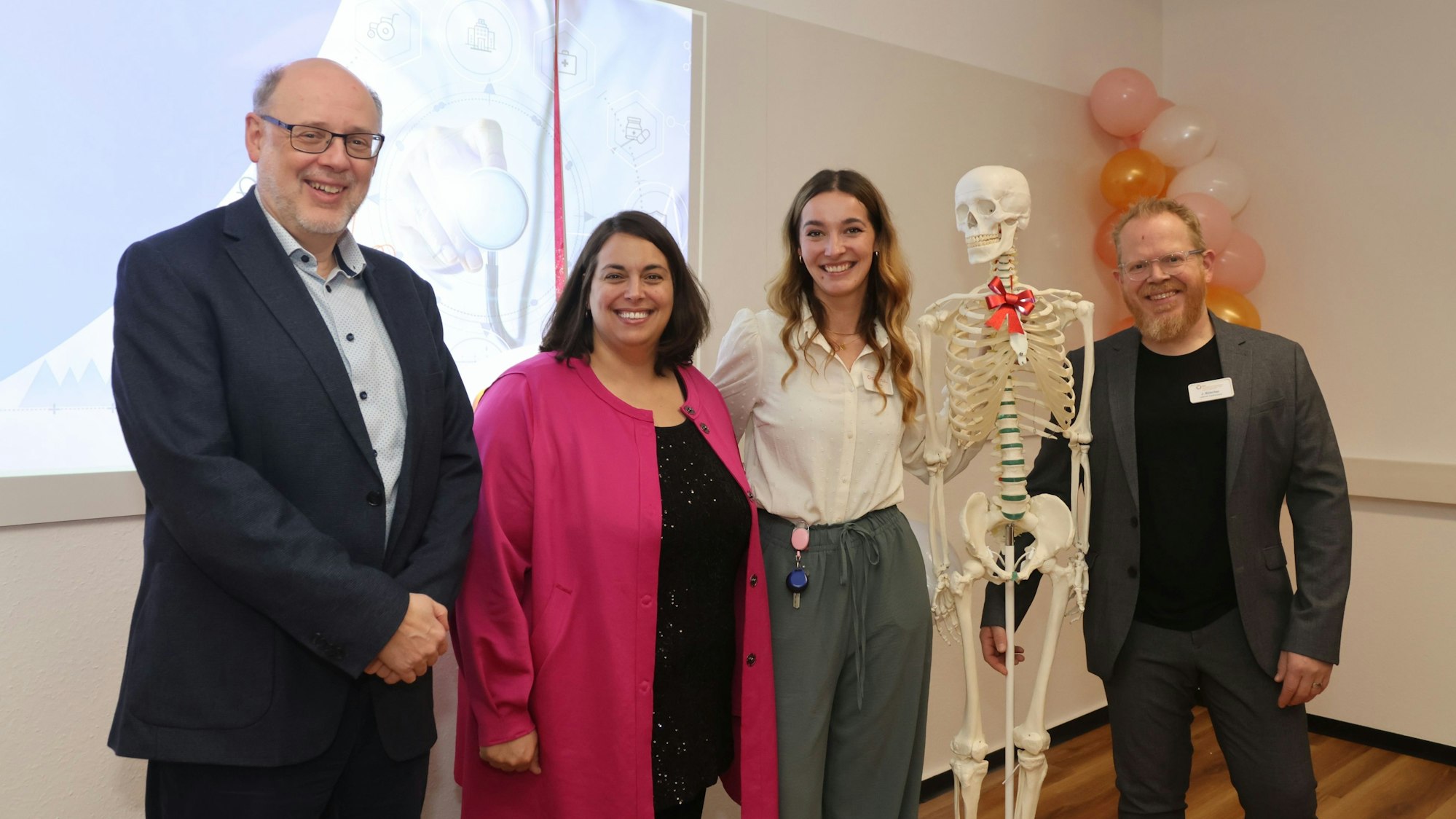 Gruppenfoto in einem Klassenzimmer. In der Mitte der Gruppe steht ein Skelett.
