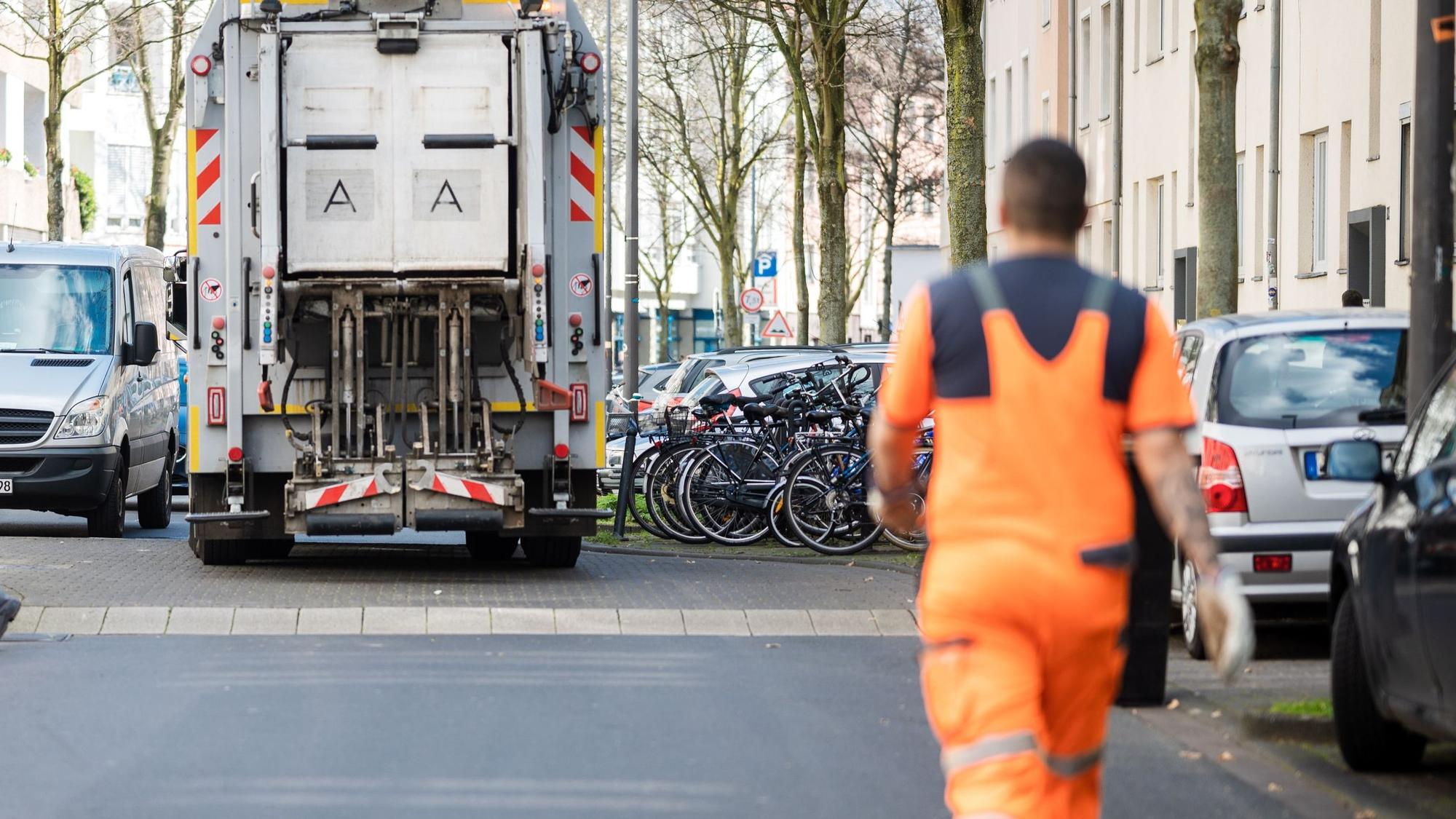 Ein Müllauto der AWB steht in einer Straße, ein Mitarbeiter der AWB läuft dem Auto hinterher.